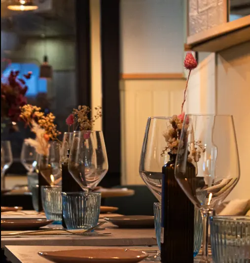 Mesas del comedor de Nakama preparadas con copas de vino, vasos y jarrones con flores secas